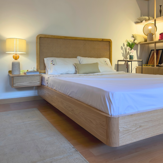 A modern bedroom featuring a Levitate Bed with a beige oak wood headboard and a low-profile bed frame, accompanied by bedside tables and lamps. The room has a minimalistic design with a white wall and wooden elements.